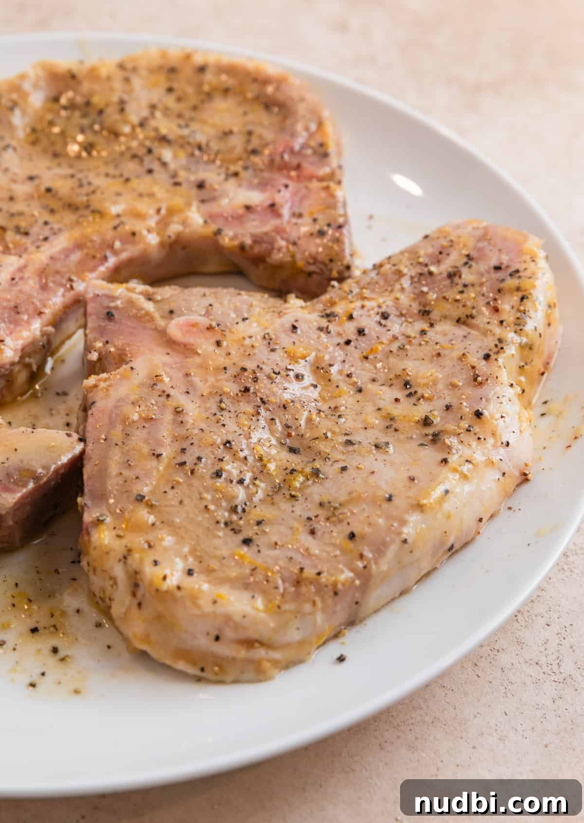 Crispy Lemon Pepper Pork Chops with Garlic Butter Sauce 6 White plate with marinaded lemon pepper pork chops before cooking.