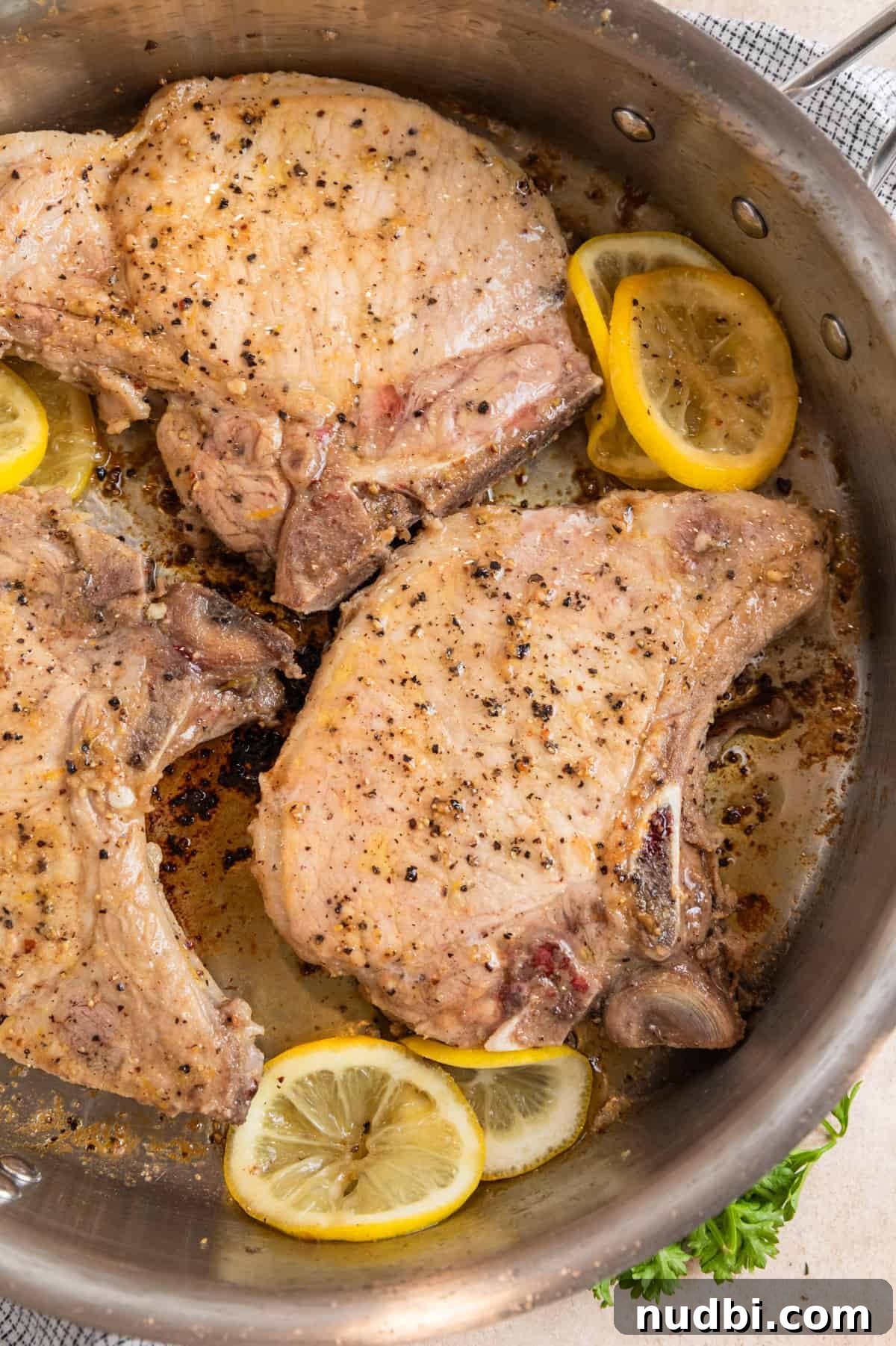 Crispy Lemon Pepper Pork Chops with Garlic Butter Sauce 7 Lemon pepper pork chops cooking in stainless steel pan with lemon slices.