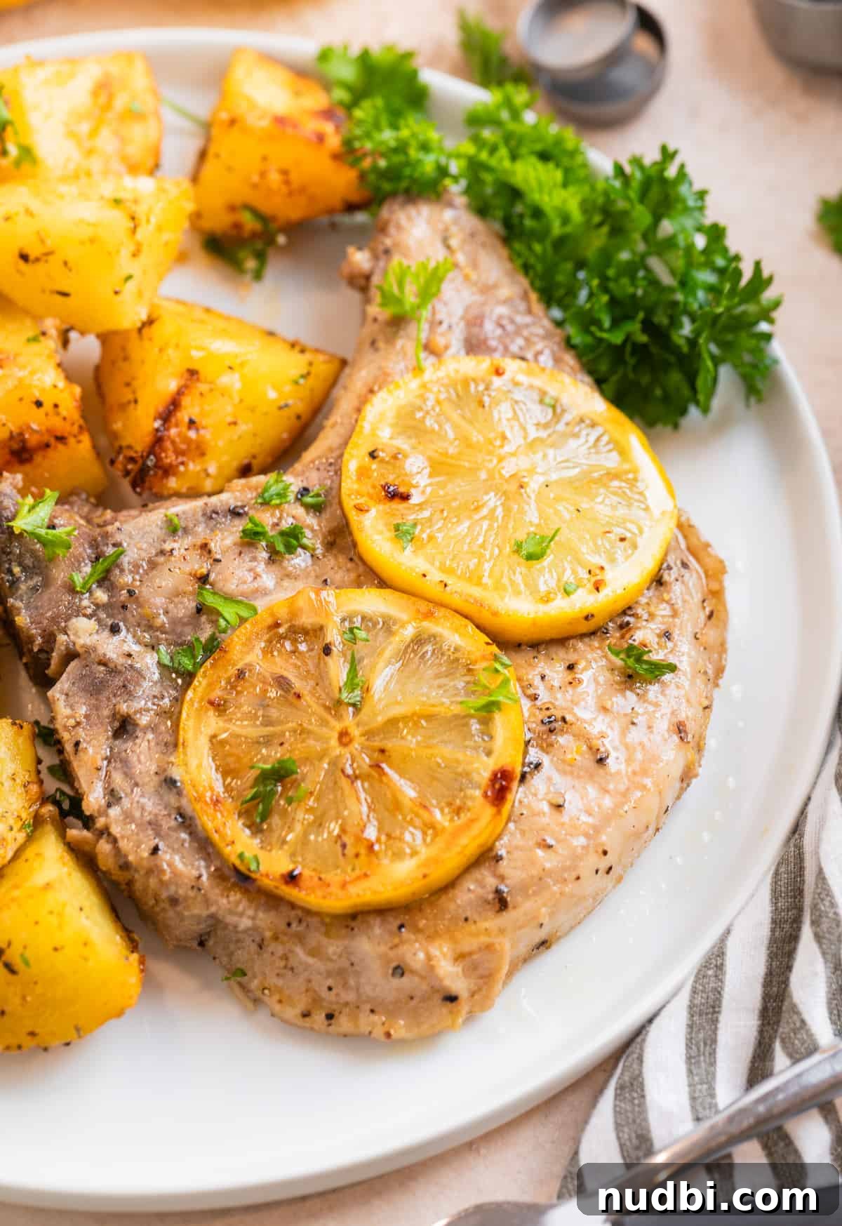 Crispy Lemon Pepper Pork Chops with Garlic Butter Sauce 8 Plate with lemon pepper pork chop with lemon slices over top.