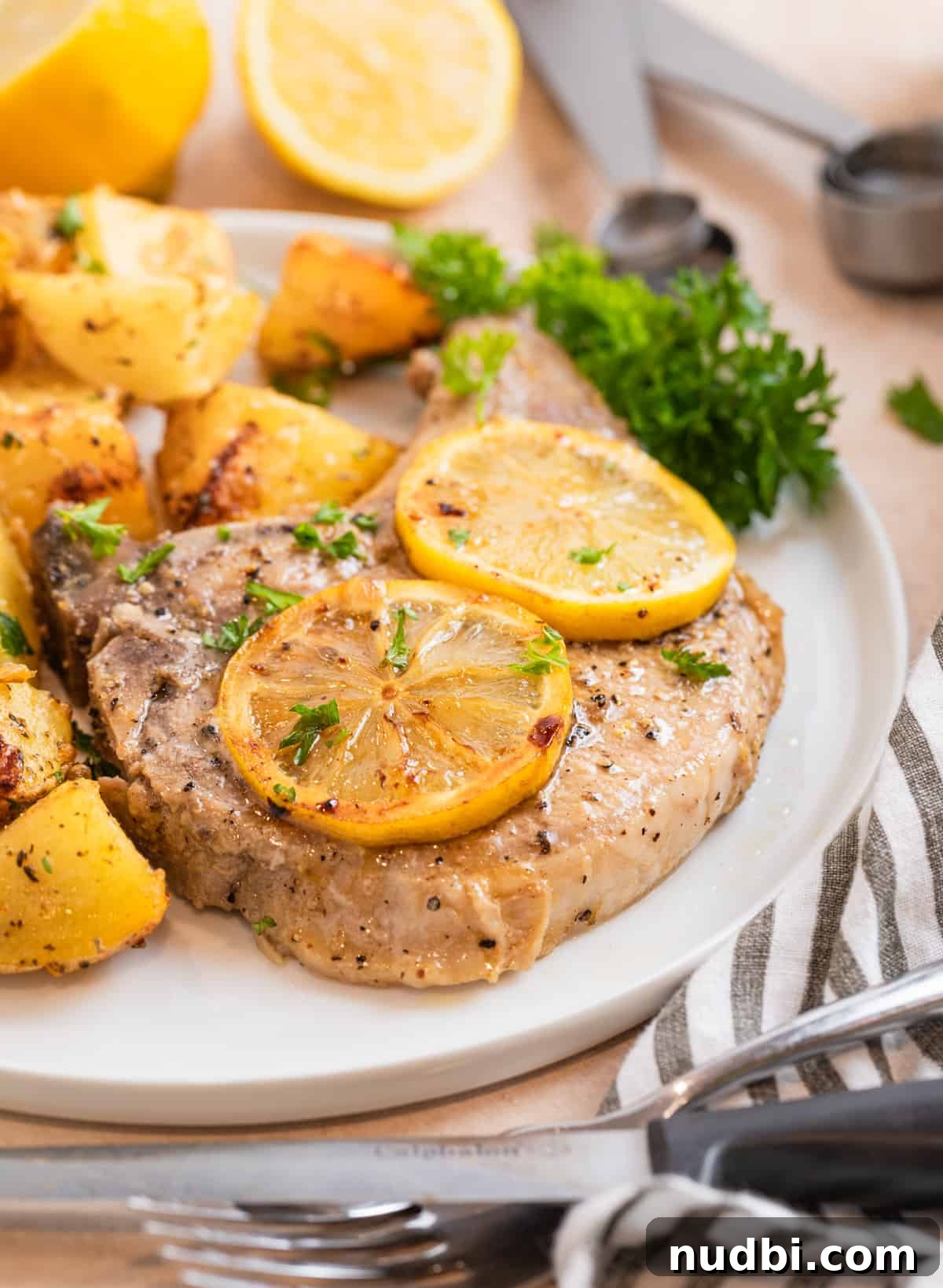 Crispy Lemon Pepper Pork Chops with Garlic Butter Sauce 9 Pork chop and potatoes on white plate with parsley and sliced lemons over top.