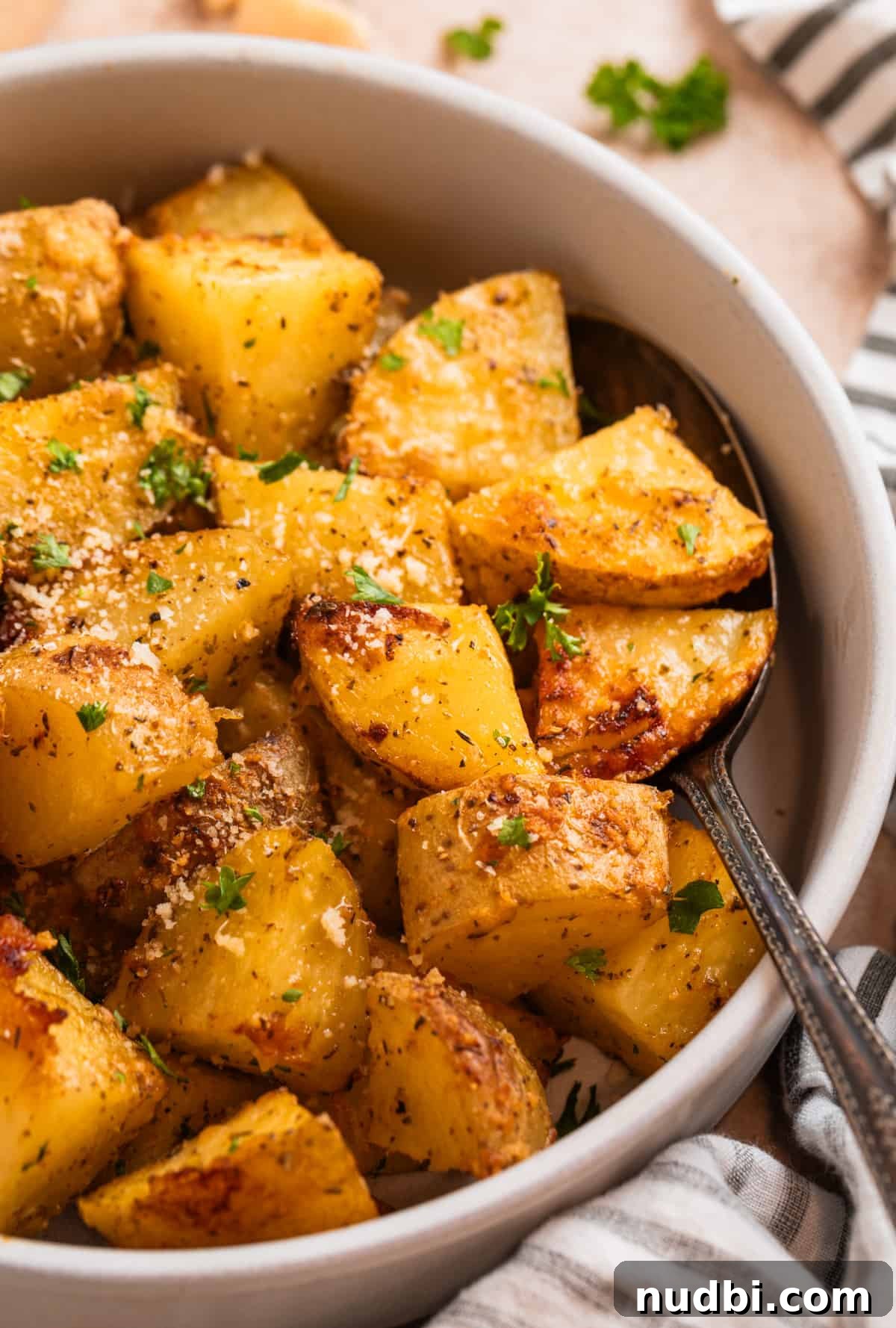 Crispy Parmesan-Crusted Potatoes with Garlic and Herbs 2 Parmesan crusted potatoes in serving bowl with freshly grated parmesan and chopped parsley on top.