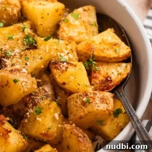 Crispy Parmesan-Crusted Potatoes with Garlic and Herbs 14 Parmesan roasted potatoes in serving dish with spoon topped with chopped fresh parsley and freshly grated parmesan.