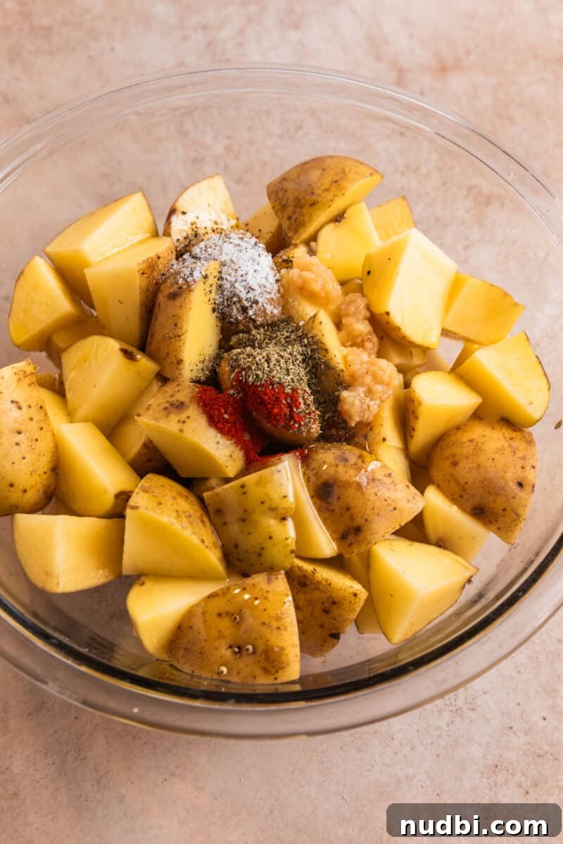 Crispy Parmesan-Crusted Potatoes with Garlic and Herbs 4 Cubed potatoes in glass bowl with salt, pepper, garlic and other seasoning poured over top.