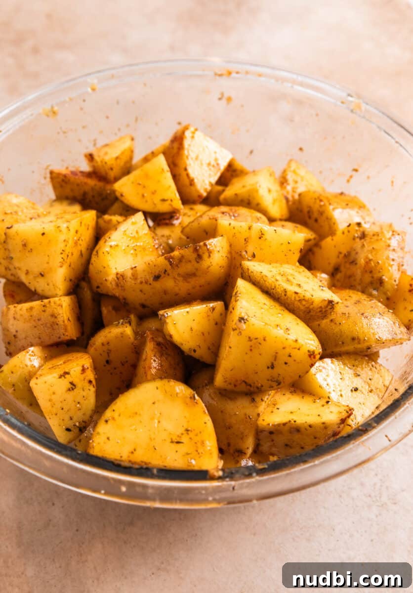Crispy Parmesan-Crusted Potatoes with Garlic and Herbs 5 Potatoes in glass bowl tossed with olive oil and seasoning.