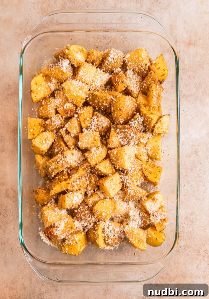 Crispy Parmesan-Crusted Potatoes with Garlic and Herbs 6 Potatoes cubed in glass baking dish topped with grated parmesan.