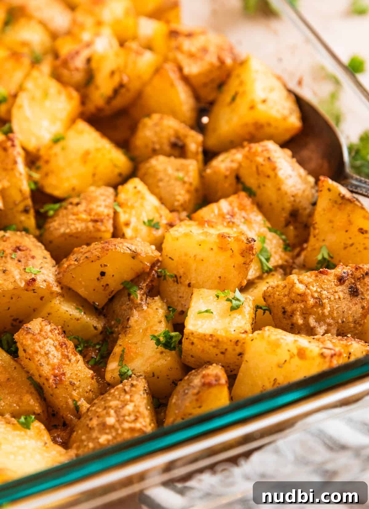 Crispy Parmesan-Crusted Potatoes with Garlic and Herbs 8 Potatoes in pan with serving spoon topped with chopped parsley.