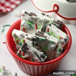 Oreo white chocolate peppermint bark in red bowl with Christmas sprinkles.