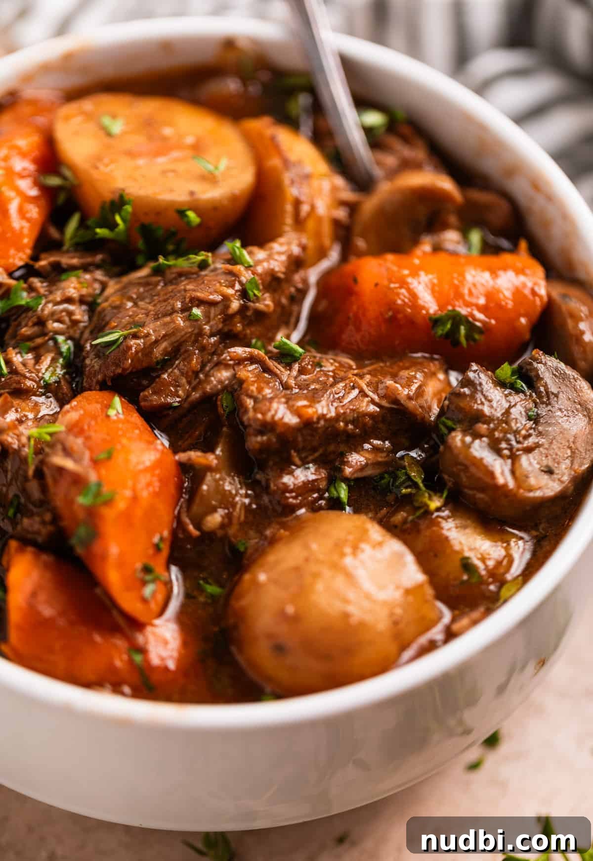 Slow Cooker Beef and Mushroom Stew Recipe for Tender Comfort Food 2 White dish with beef stew with potatoes, carrots, mushrooms and onion topped with parsley.