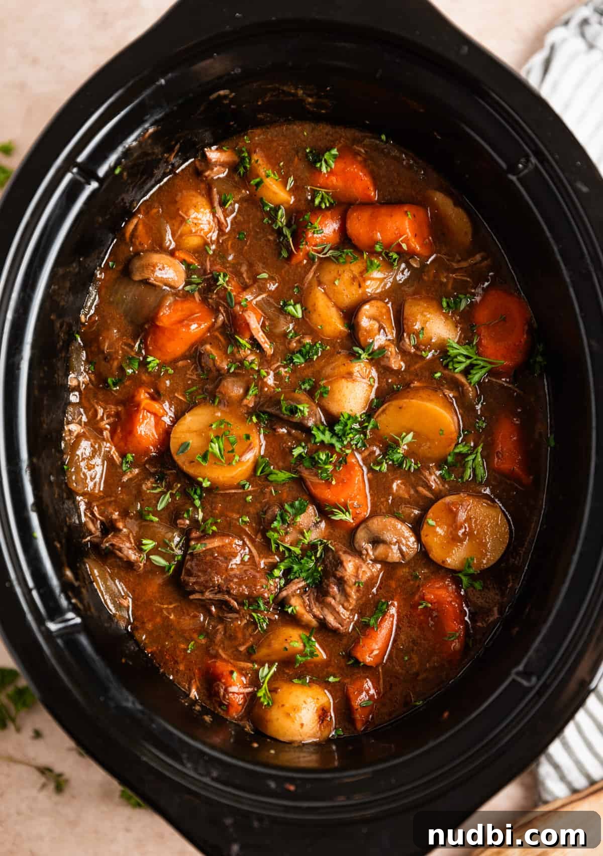Slow Cooker Beef and Mushroom Stew Recipe for Tender Comfort Food 13 Beef and mushroom stew in slow cooker with potatoes and carrots and topped with parsley.