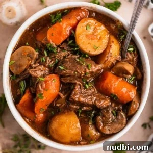 Slow Cooker Beef and Mushroom Stew Recipe for Tender Comfort Food 15 White bowl with crockpot beef stew with mushrooms, carrots and potatoes topped with chopped parsley.
