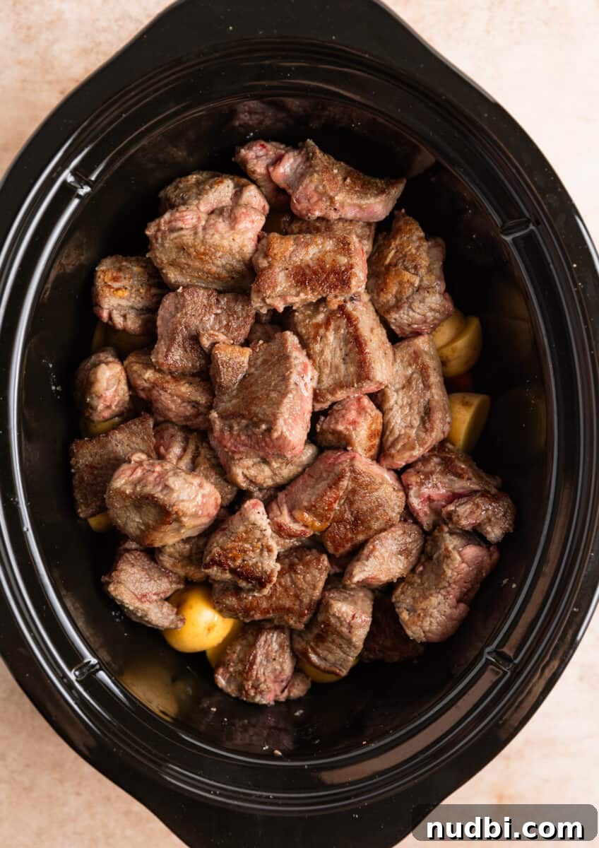 Slow Cooker Beef and Mushroom Stew Recipe for Tender Comfort Food 9 Seared beef over carrots and potato chunks in crockpot.
