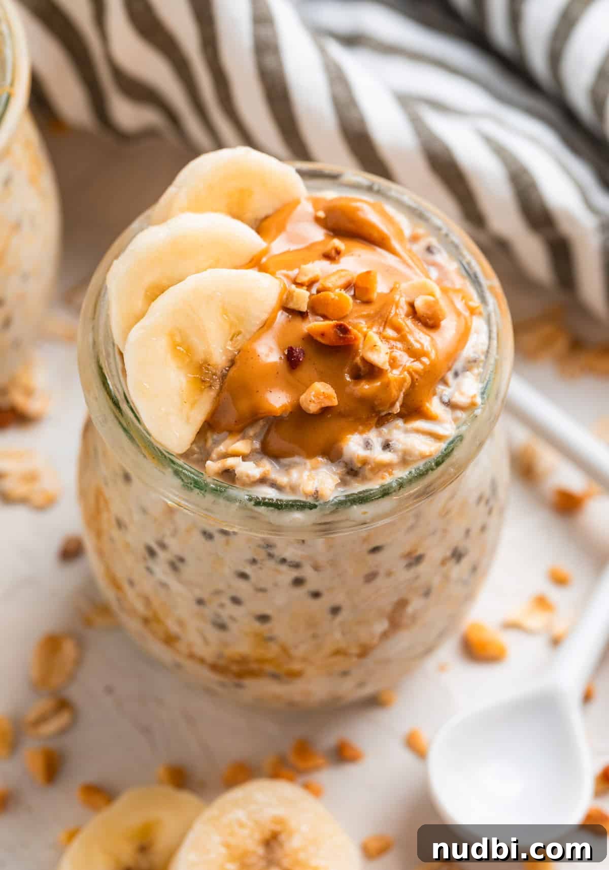 High-Protein Overnight Oats Recipe for Busy Mornings 2 Peanut butter topped oatmeal in jar with sliced bananas and topped with chopped nuts.