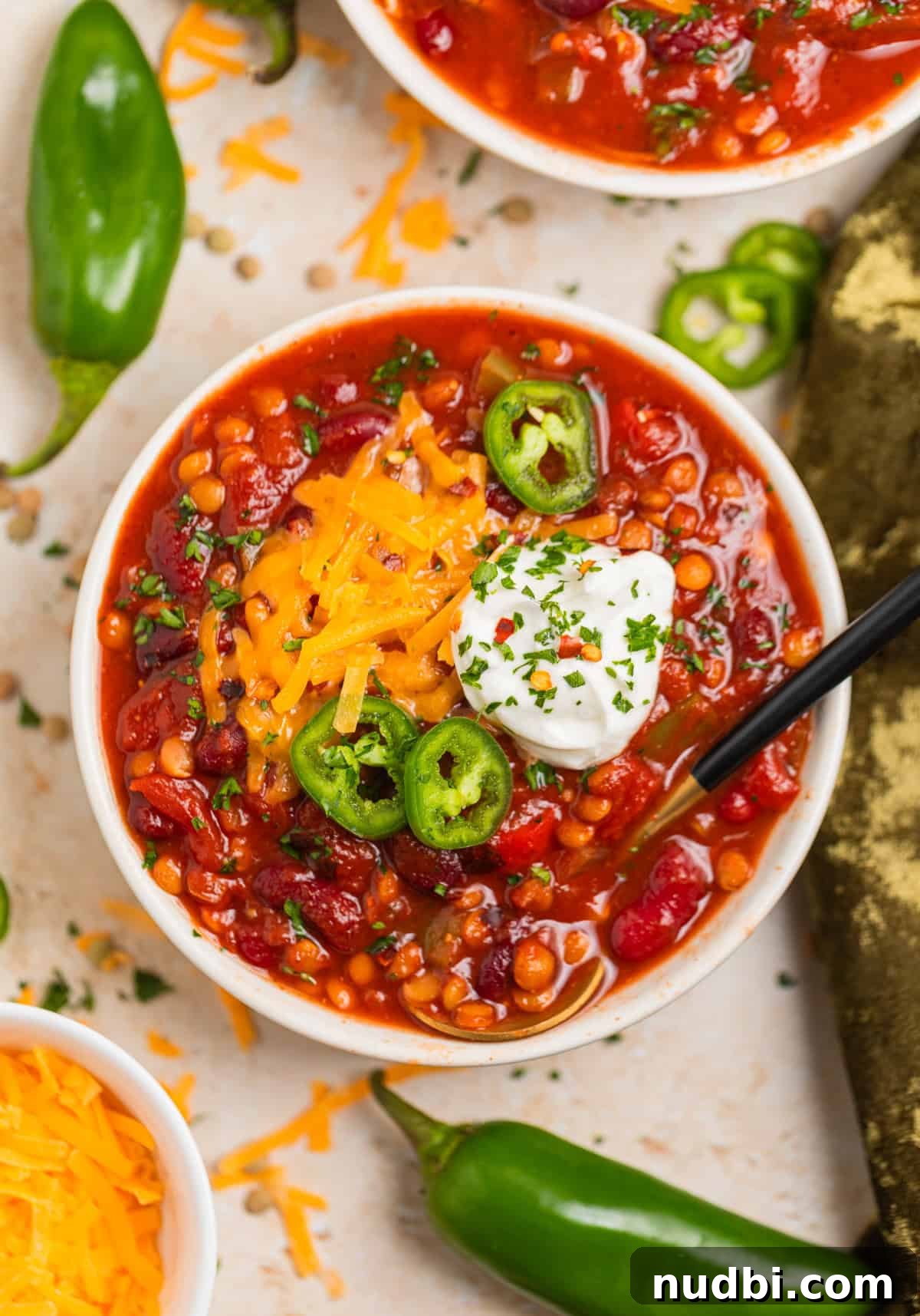 Slow-Cooker Lentil Chili Recipe for Comforting Weeknight Meals 2 Slow cooker lentil chili served in a bowl with spoon and topped with sour cream, cheese and jalapeño.
