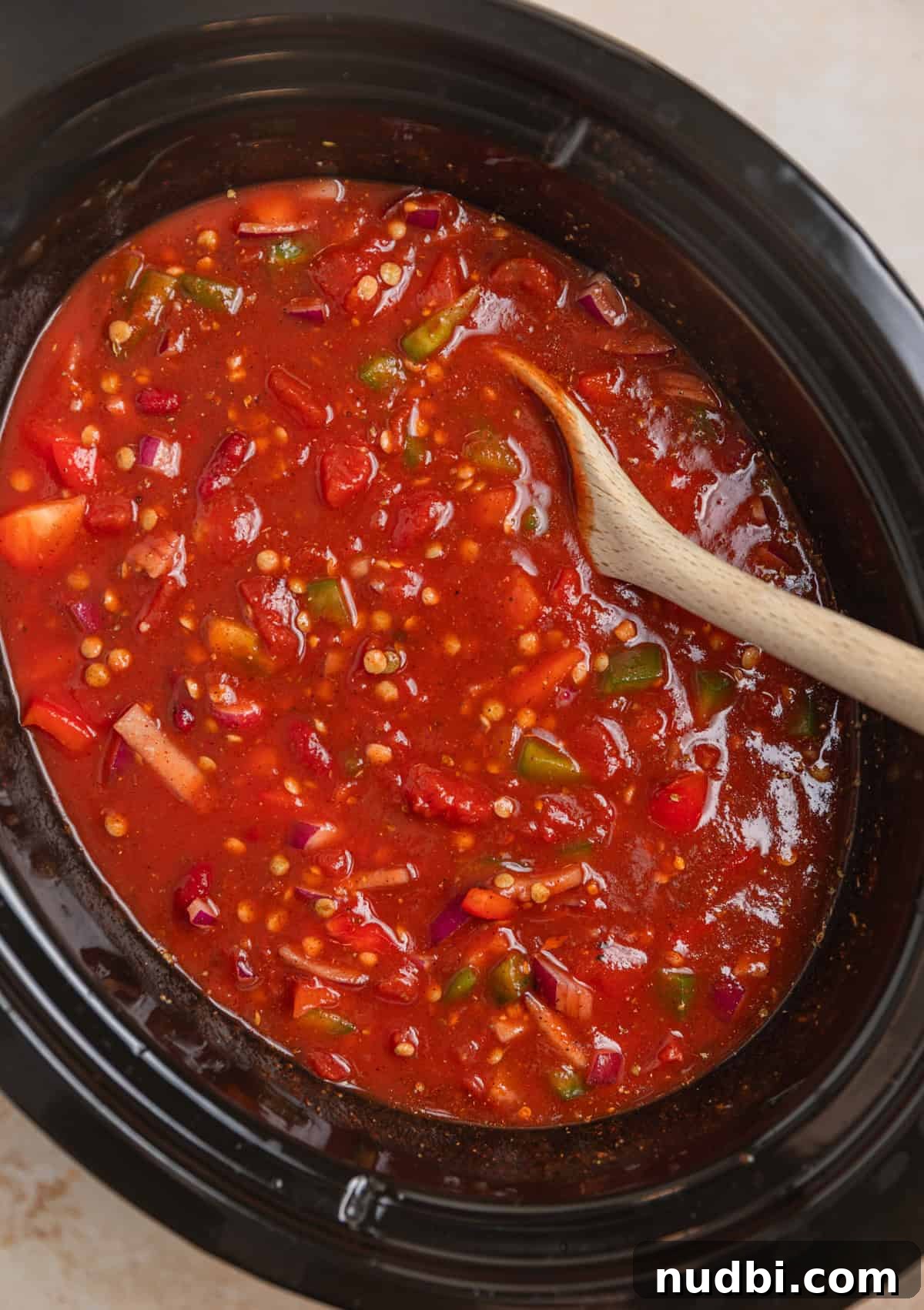 Slow-Cooker Lentil Chili Recipe for Comforting Weeknight Meals 4 Lentil chili ingredients stirred together in slow cooker pot with wooden spoon before cooking.