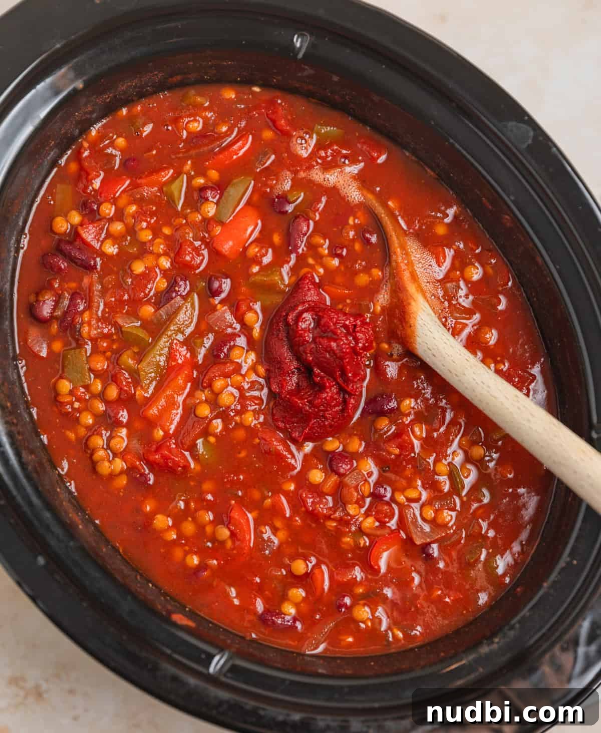 Slow-Cooker Lentil Chili Recipe for Comforting Weeknight Meals 5 Lentil chili ingredients stirred together in slow cooker pot with wooden spoon before cooking with tomato paste added on top.