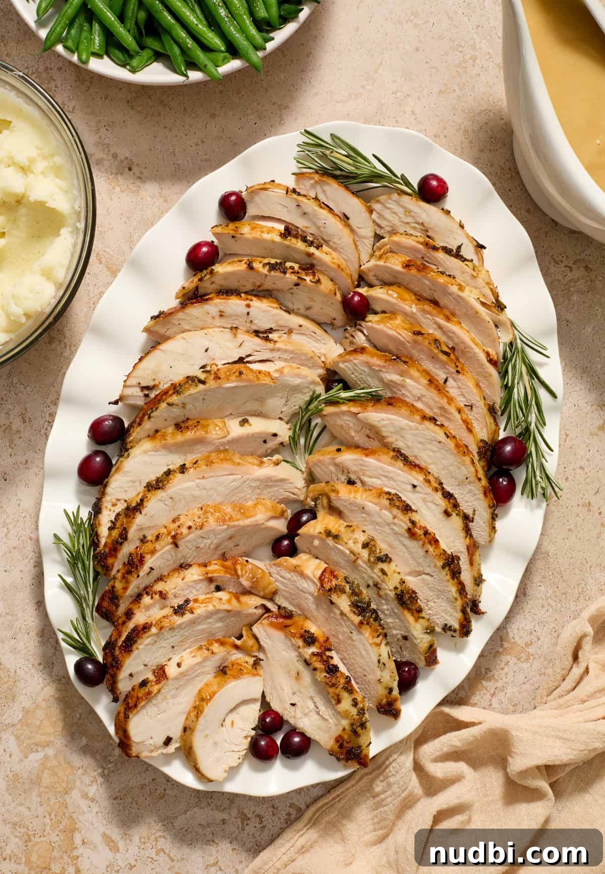 Juicy Slow Cooker Turkey Breast Recipe 2 Sliced turkey breast on serving plate with rosemary and cranberry garnish.