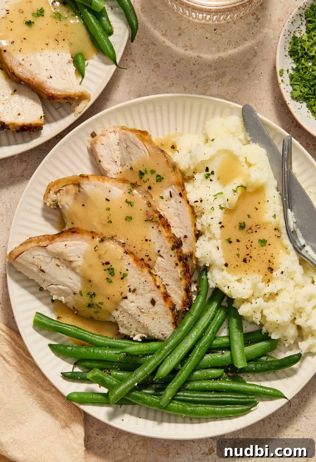 Juicy Slow Cooker Turkey Breast Recipe 3 Slices of turkey with gravy, cooked green beans and mashed potatoes on plate with fork and knife.