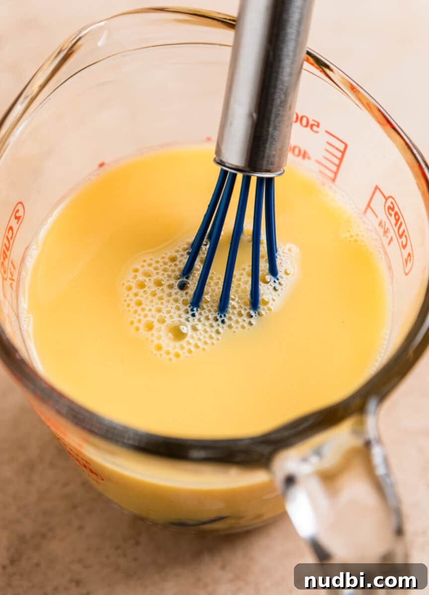 Turkey Sausage Stuffing Recipe for Thanksgiving and Holiday Meals 12 Egg and broth whisked together in glass measuring cup with whisk sitting in mixture.