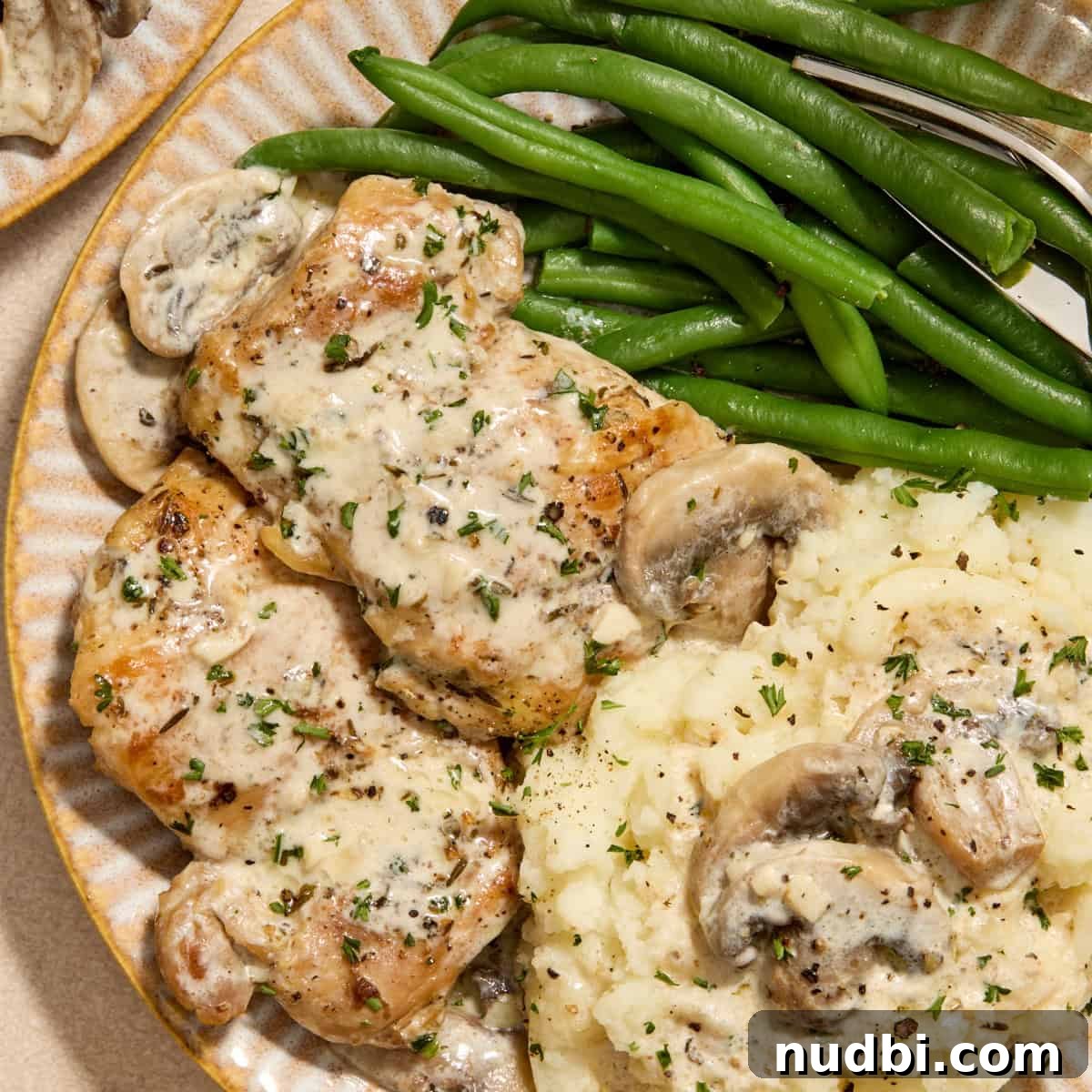 Plate with creamy chicken thighs and mushrooms with mashed potatoes and green beans.