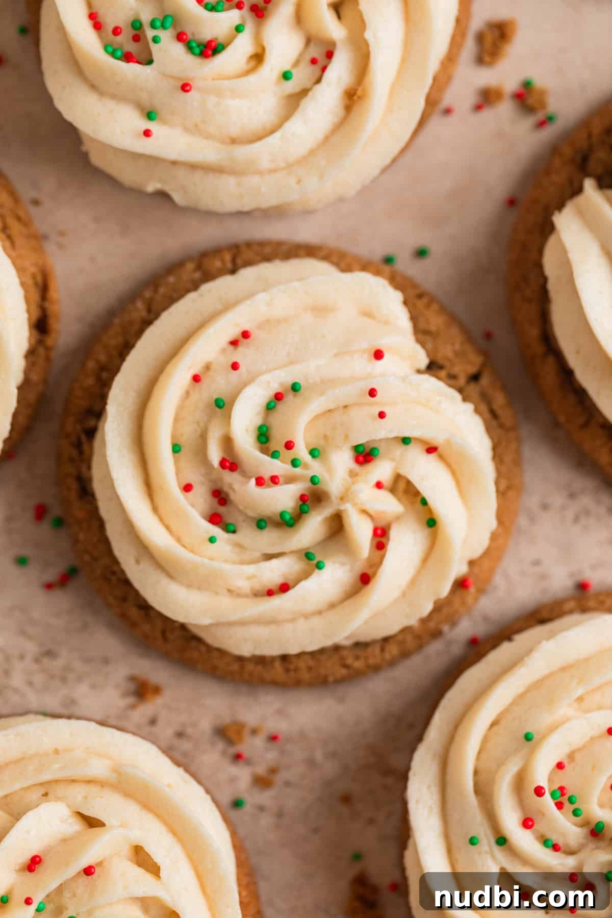 Chewy Ginger Cream Cookie Recipe for Perfect Holiday Baking 14 Frosted ginger cookies with sprinkles arranged on surface with cookie crumbs.