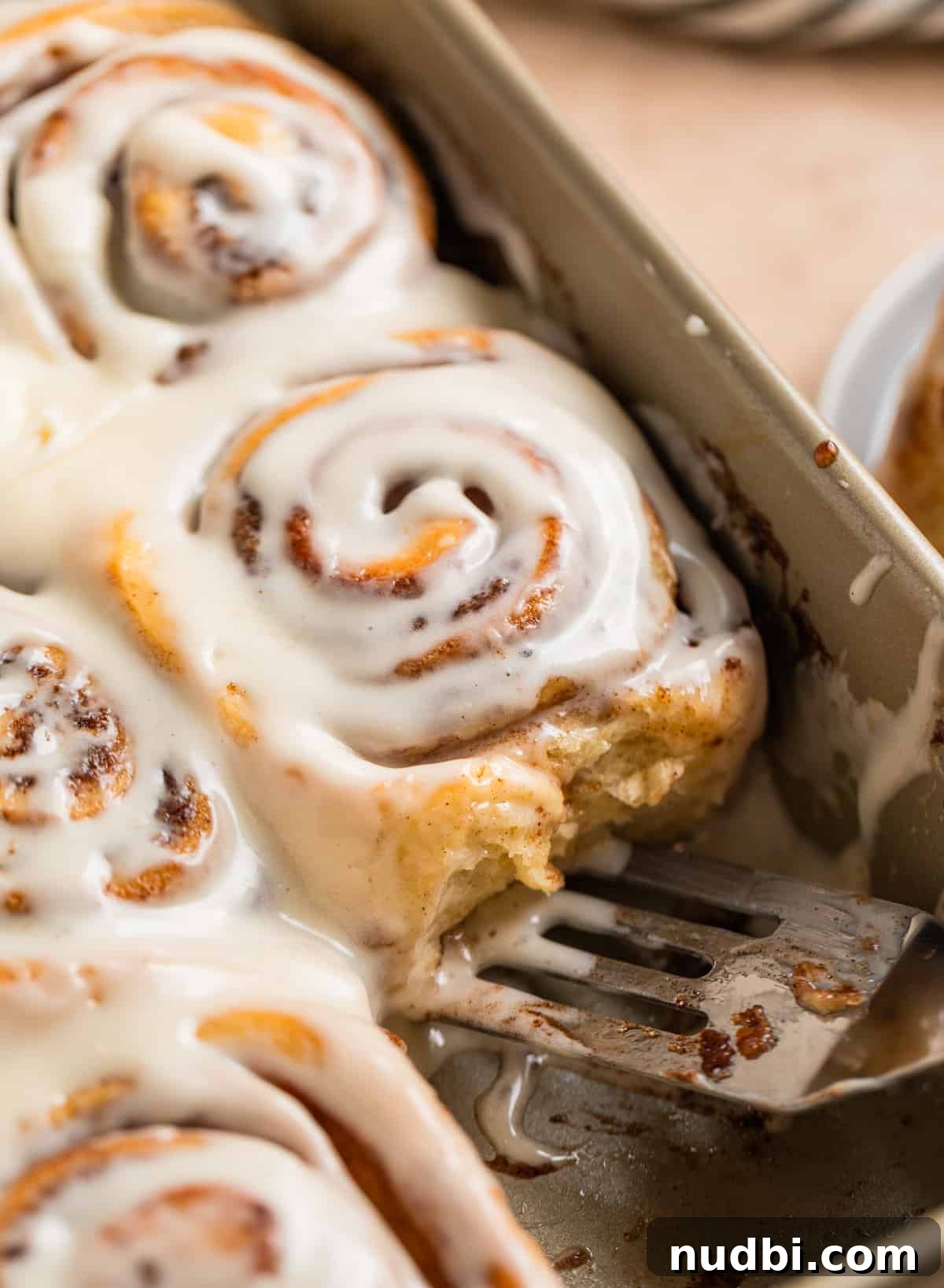 Fluffy Buttermilk Cinnamon Rolls from Scratch 3 Iced buttermilk cinnamon rolls in pan with spatula scooping into the pan.