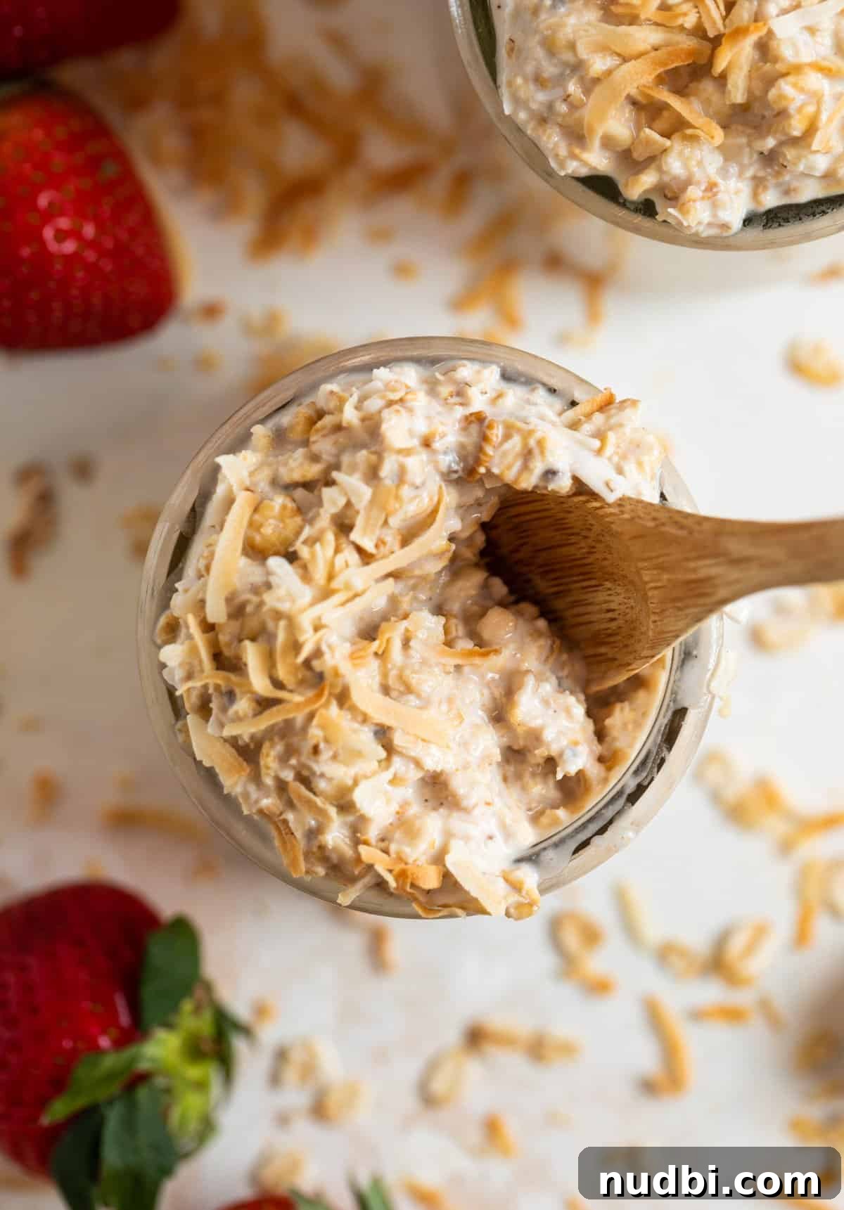 Coconut Cream Pie Overnight Oats Recipe for Creamy Breakfast 3 Wood spoon scooped in coconut overnight oats with oats and coconut surrounding.