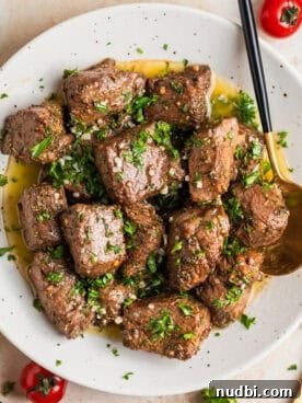 White plate with air fryer steak bites in lemon garlic butter sauce with fresh parsley over top.
