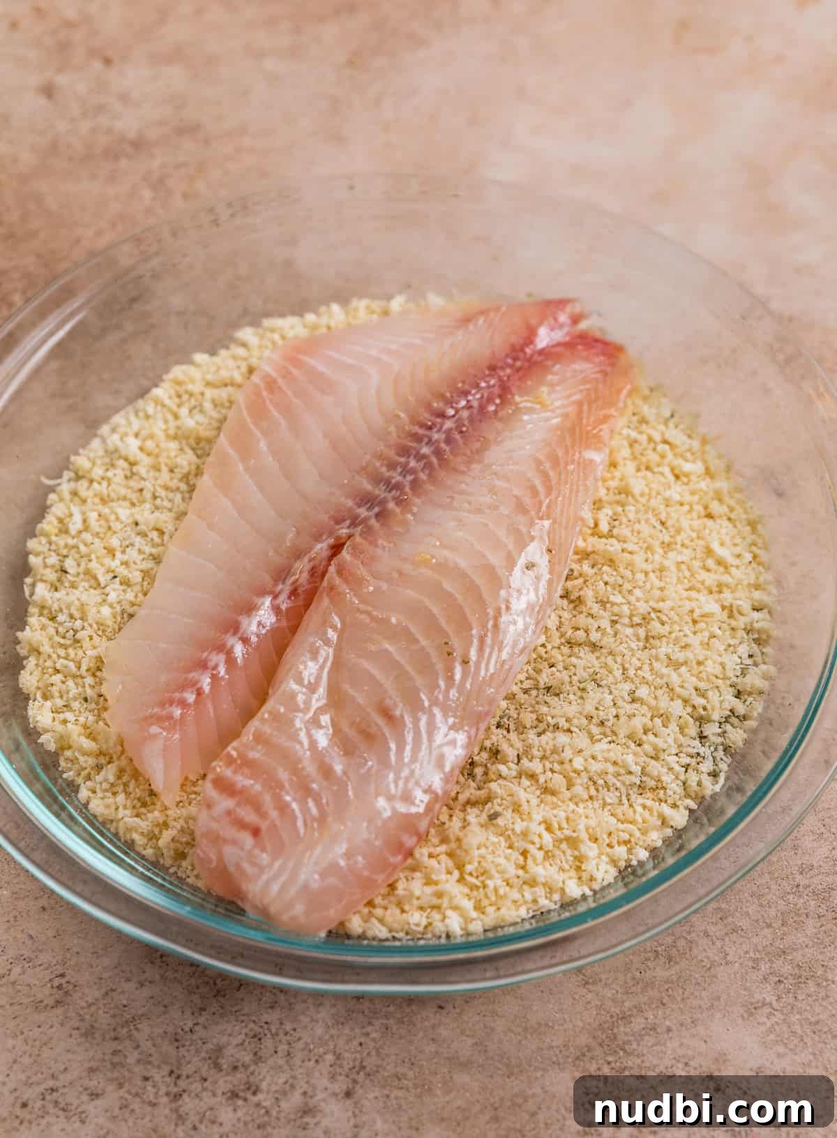 Crispy Parmesan-Crusted Tilapia in the Air Fryer 4 Tilapia added to breadcrumb mixture in dish.