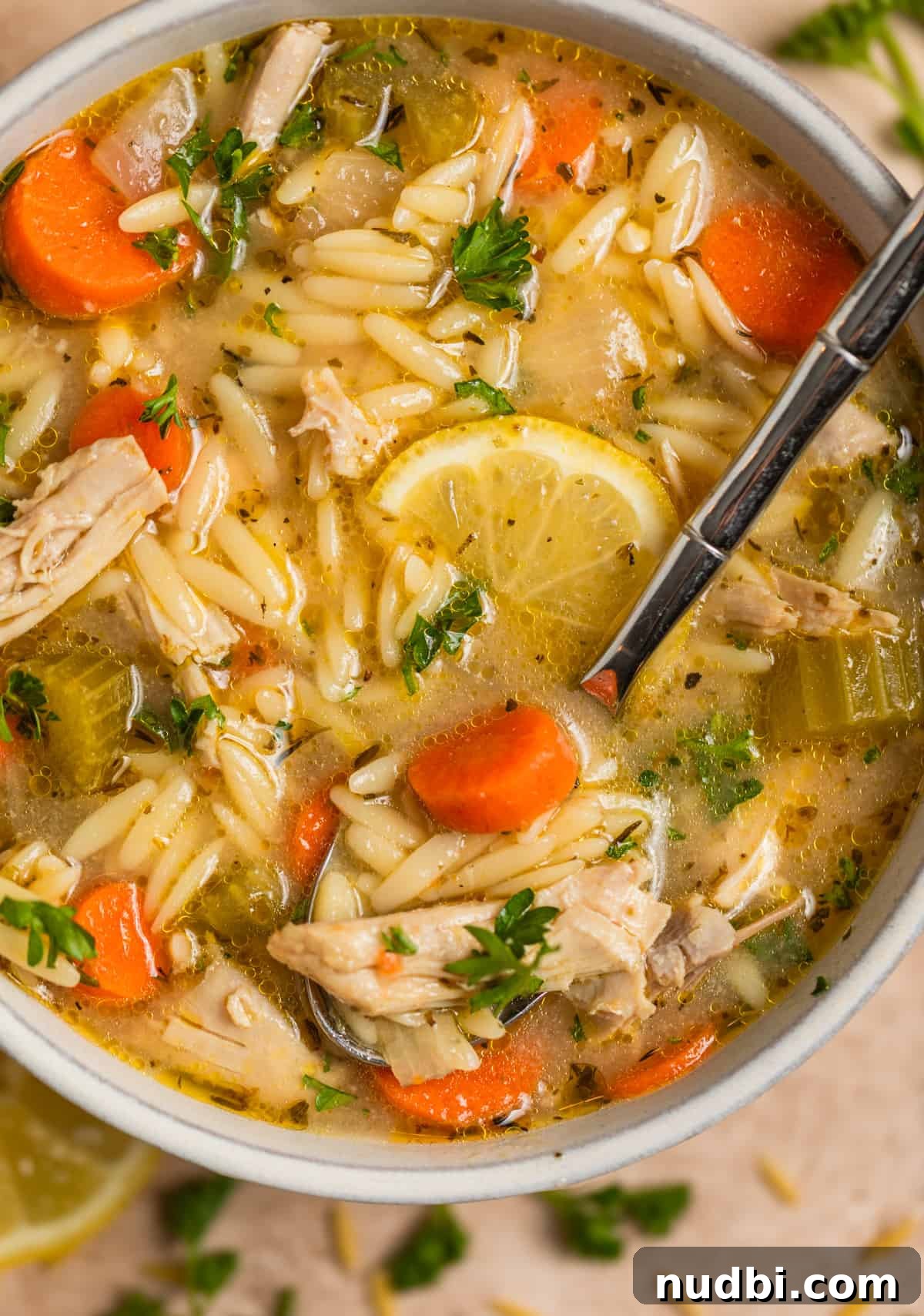 Lemony Chicken Orzo Soup Recipe for Comforting Weeknights 2 Chicken lemon orzo soup in bowl with spoon scooping in and topped with lemon slices and chopped parsley.