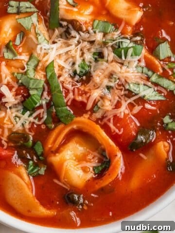 White bowl with tomato tortellini soup and spoon scooping in.