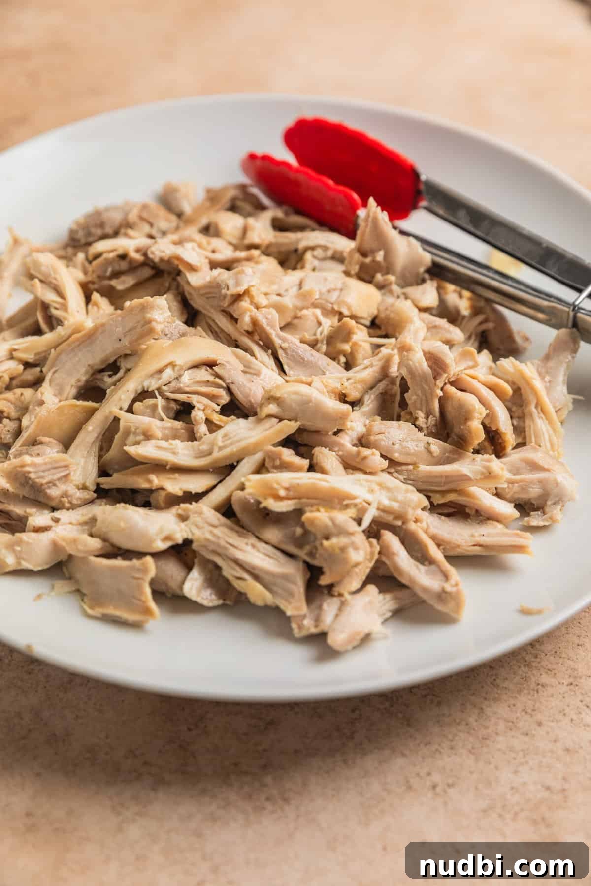 Lemony Chicken Orzo Soup Recipe for Comforting Weeknights 6 Shredded chicken thighs on white plate with tongs.