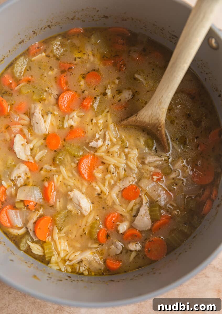 Lemony Chicken Orzo Soup Recipe for Comforting Weeknights 7 Chicken added to lemon chicken orzo soup with wooden spoon.