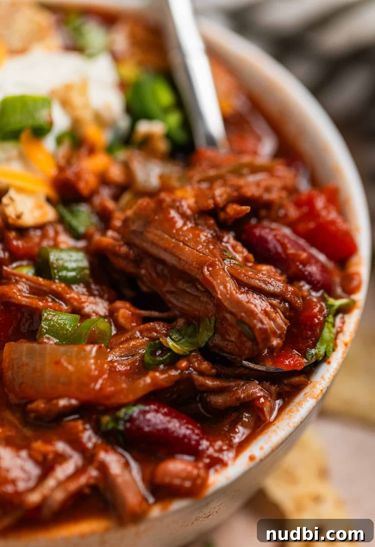 Slow Cooker Shredded Beef Chili Recipe for Comforting Weeknights 2 Bowl of shredded beef chili with spoon scooping into it.