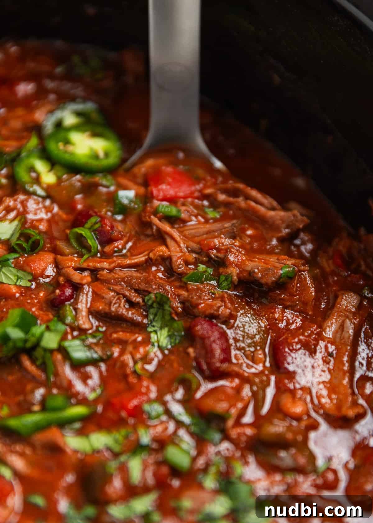 Slow Cooker Shredded Beef Chili Recipe for Comforting Weeknights 9 Slow cooker shredded beef chili in crockpot topped with cilantro and jalapeño with ladle.