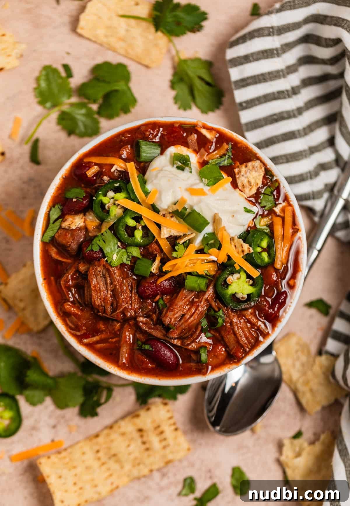 Slow Cooker Shredded Beef Chili Recipe for Comforting Weeknights 10 Overhead view of chili in bowl topped with sour cream, cheese, cilantro and other toppings.