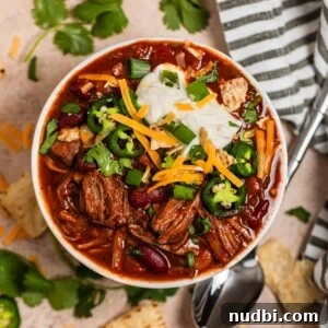 Slow Cooker Shredded Beef Chili Recipe for Comforting Weeknights 15 Overhead view of shredded beef chili topped with sour cream, cilantro, cheese and more.