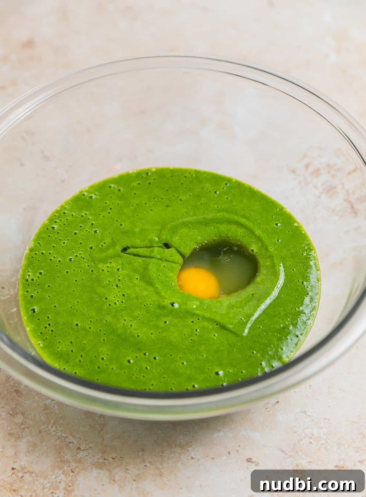 Glass mixing bowl with spinach and banana mixture and egg added to it.
