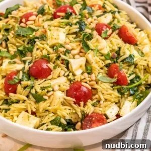 Pesto orzo salad in white bowl topped with freshly chopped basil and toasted pine nuts.