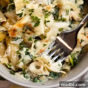 Chicken spinach and artichoke pasta casserole in dish with fork.