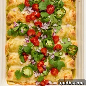 Pan of green chicken enchiladas topped with onion, cilantro, tomatoes, etc.