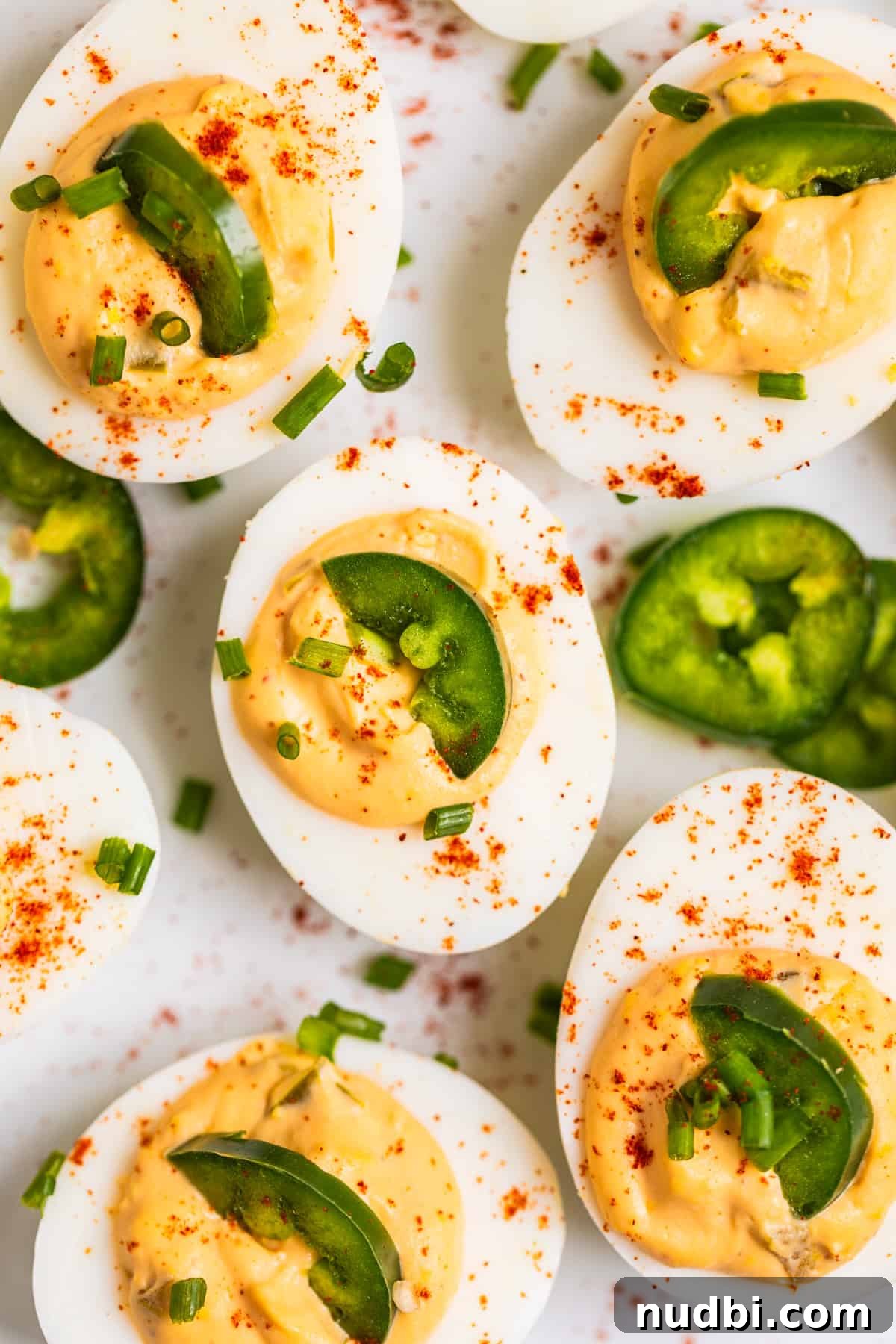 Spicy Deviled Eggs Recipe with Tangy Jalapeño Kick 2 White dish with spicy deviled eggs topped with half slice of jalapeño and a sprinkle of paprika and chives.