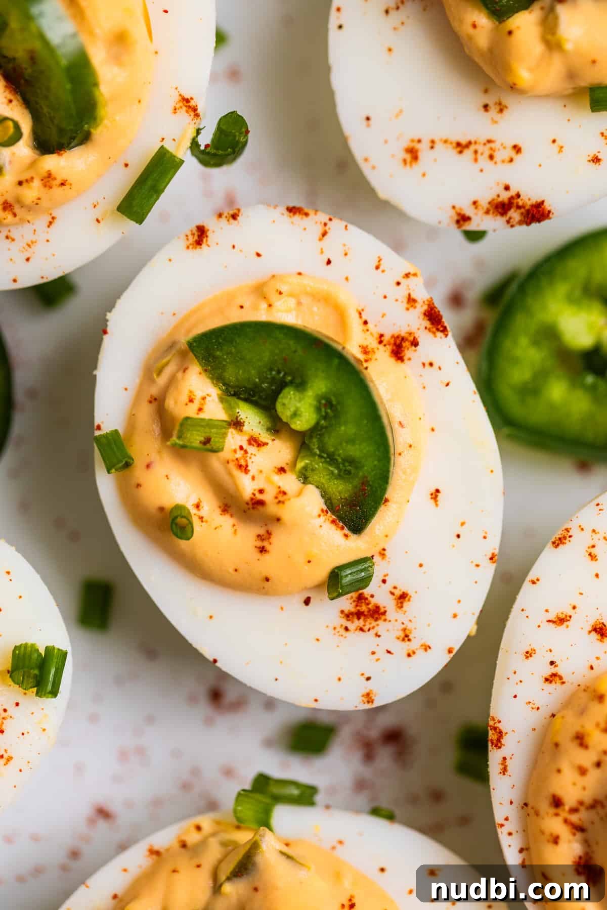 Spicy Deviled Eggs Recipe with Tangy Jalapeño Kick 3 Close up view of spicy deviled egg on plate with slice of jalapeño and paprika on top.