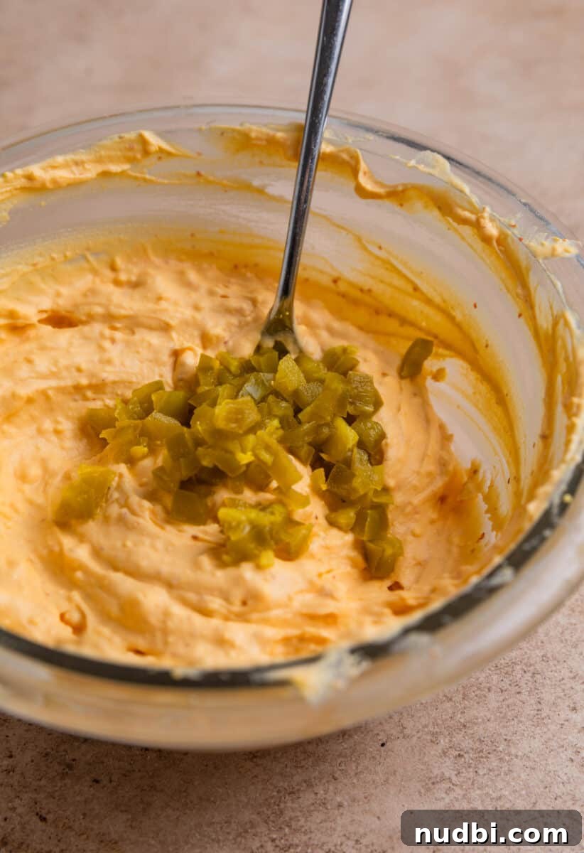 Spicy Deviled Eggs Recipe with Tangy Jalapeño Kick 7 Deviled egg filling mixture in glass mixing bowl with chopped jalapeño over top.