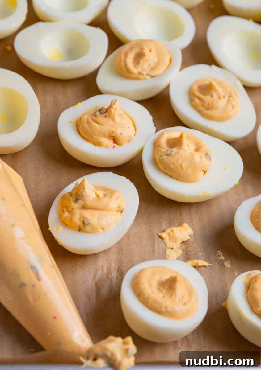 Spicy Deviled Eggs Recipe with Tangy Jalapeño Kick 9 Boiled egg halves filled with egg yolk mixture with piping bag of yolk mixture beside them.