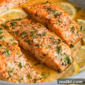 Lemon dill seared salmon in skillet with extra chopped dill on top and lemon slices.
