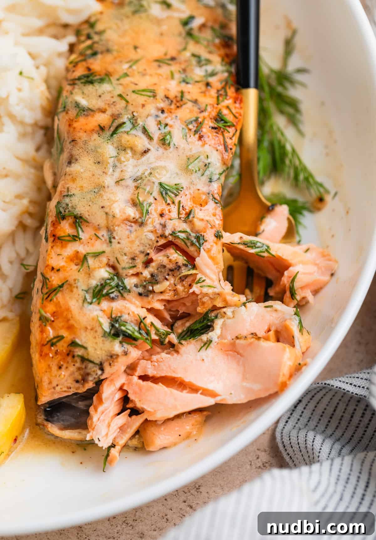 Salmon filet flaked with fork on plate topped with lemon dill butter.