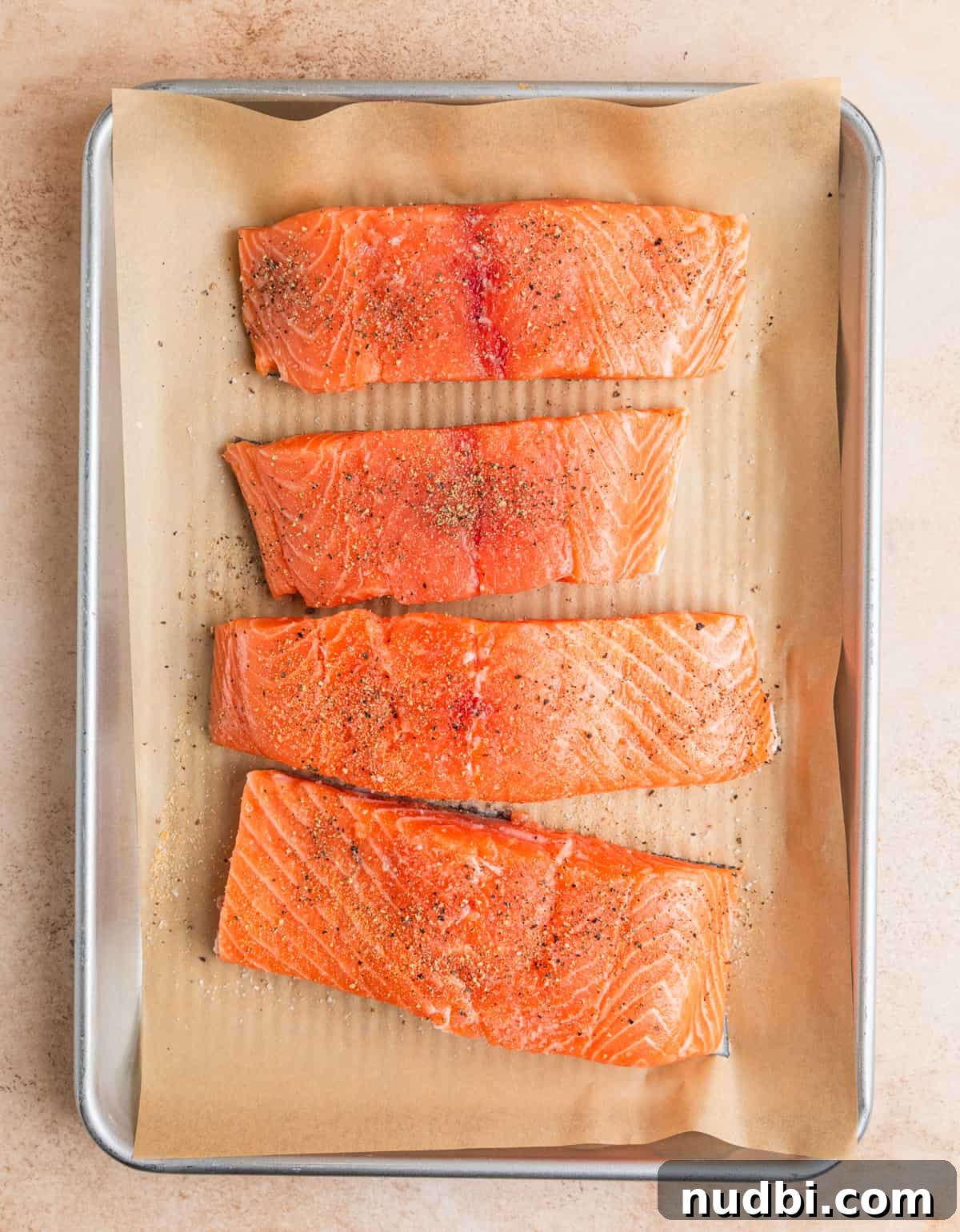 Raw salmon filets on parchment lined pan with seasoning.
