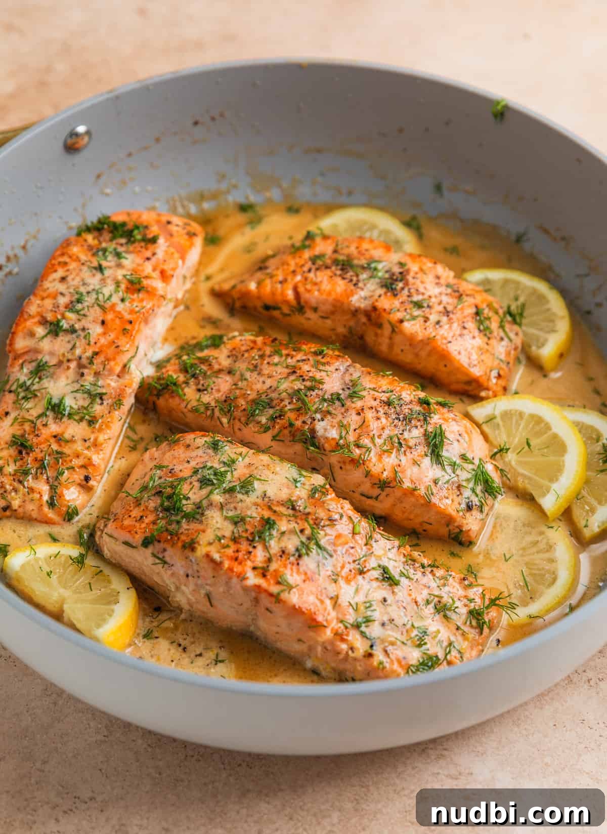 Cooked lemon dill salmon in pan with lemon slices and butter sauce.