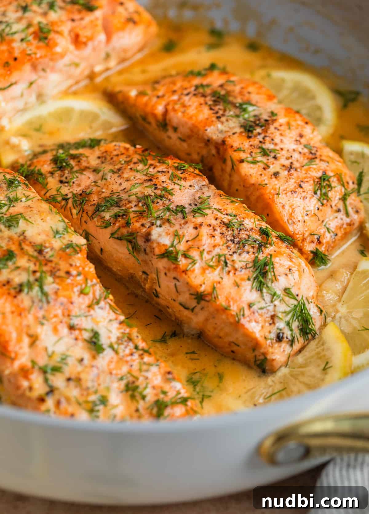 Salmon in skillet with lemons and topped with chopped dill.