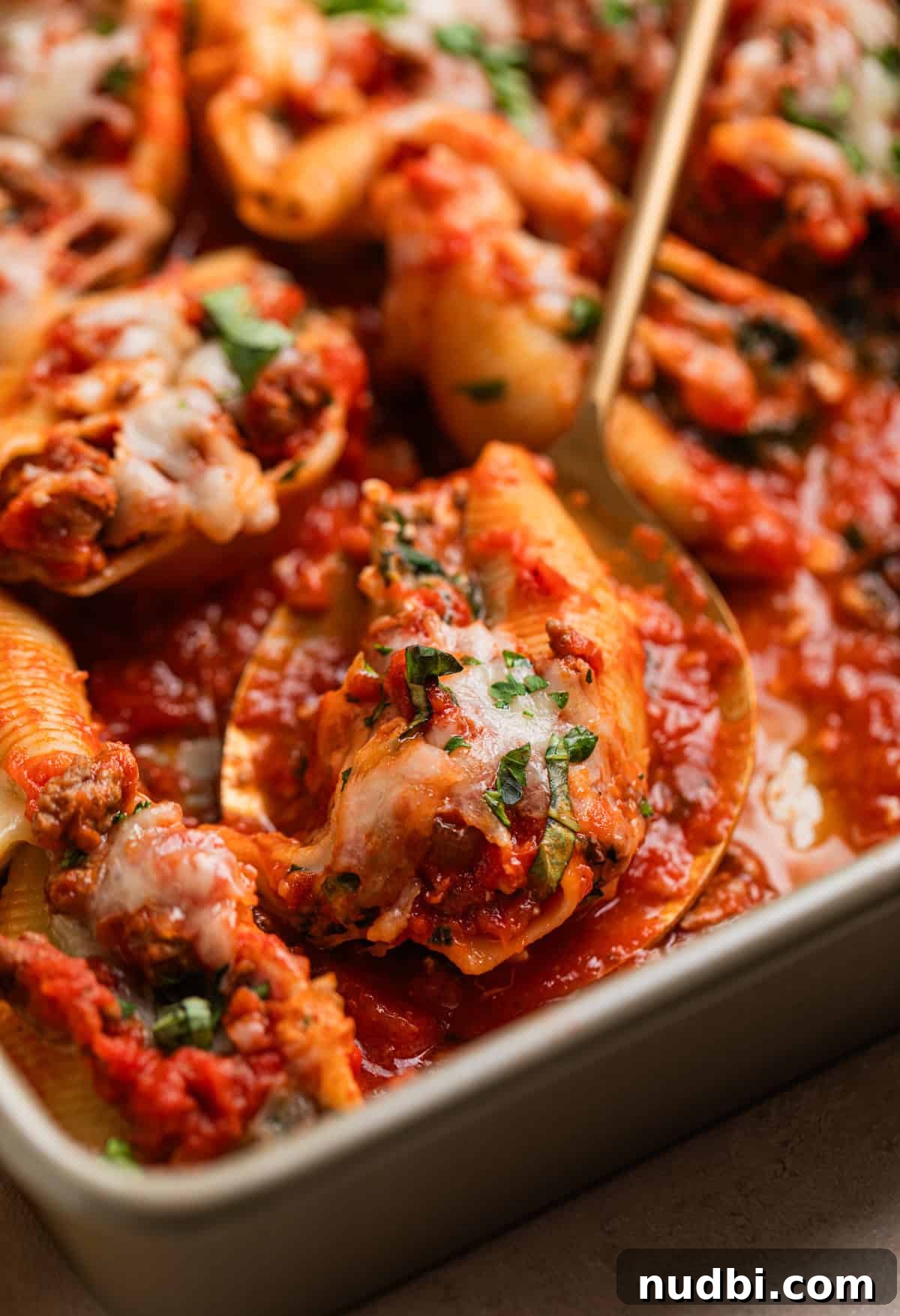 Cheesy Ground Beef Stuffed Shells Recipe for Family Dinners 8 Spoon with beef stuffed shell on it topped with melted cheese and chopped parsley and basil.